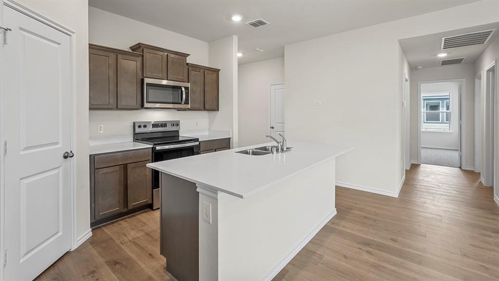 Kitchen featuring dark wood-finish cabinetry, quartz countertops, a central island with a double-basin sink, stainless steel appliances, and wood-finish flooring