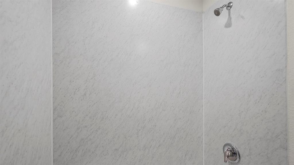 Shower enclosure featuring light-toned, veined wall panels and a polished chrome shower head and single-handle mixing valve Shower enclosure featuring light-toned, veined wall panels and a polished chrome shower head and single-handle mixing valve