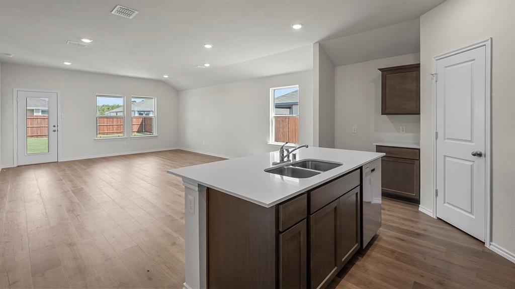 Open-concept interior featuring wood-finish flooring, recessed lighting, a center kitchen island with a quartz countertop, and dark-toned cabinetry