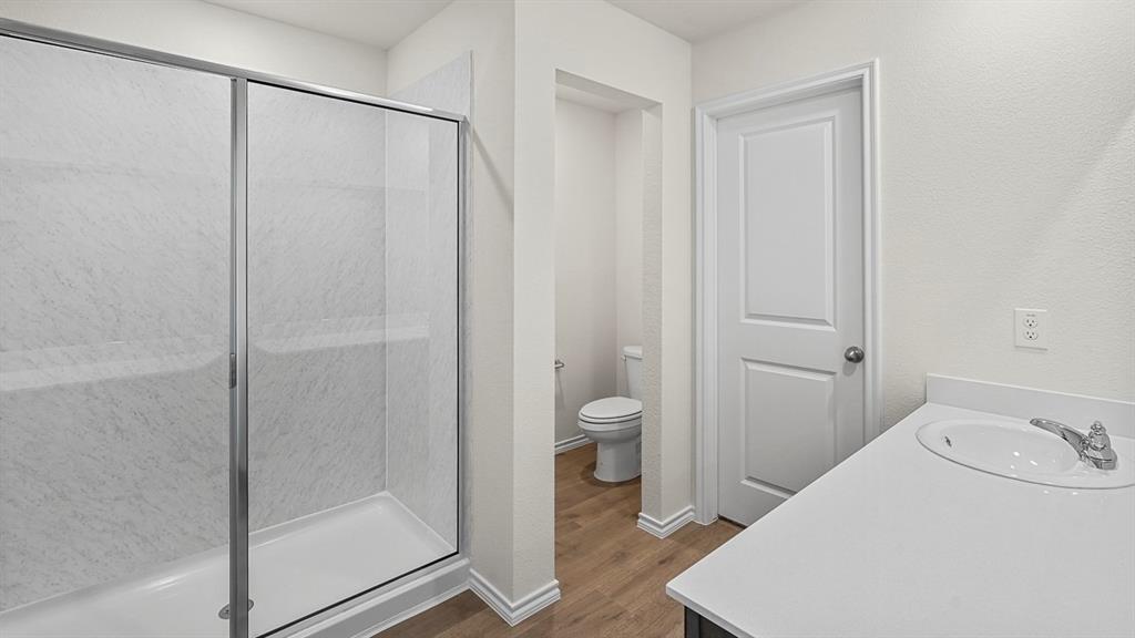 Shower featuring a glass sliding enclosure and stone-patterned surround, stone-surface vanity countertop with an integrated oval sink, and wood-finish flooring