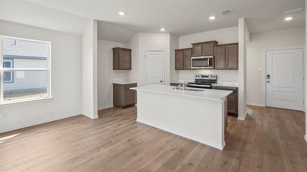 Kitchen featuring wood-finish cabinetry, white countertops, an island with a stainless steel sink, recessed lighting, and wood-finish flooring