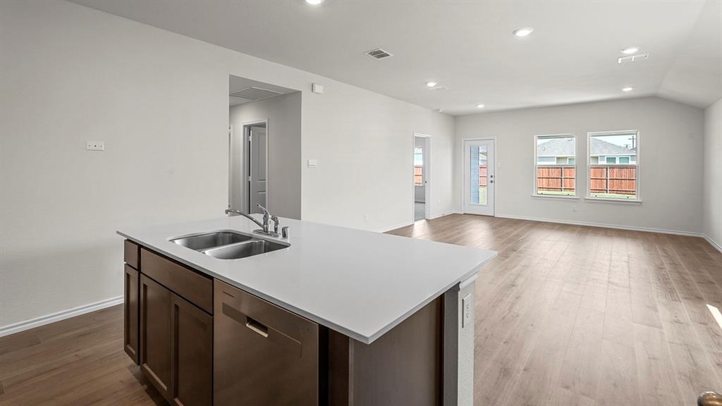 Kitchen island featuring stone countertops, a stainless steel dual-basin sink, and dark-finish cabinetry