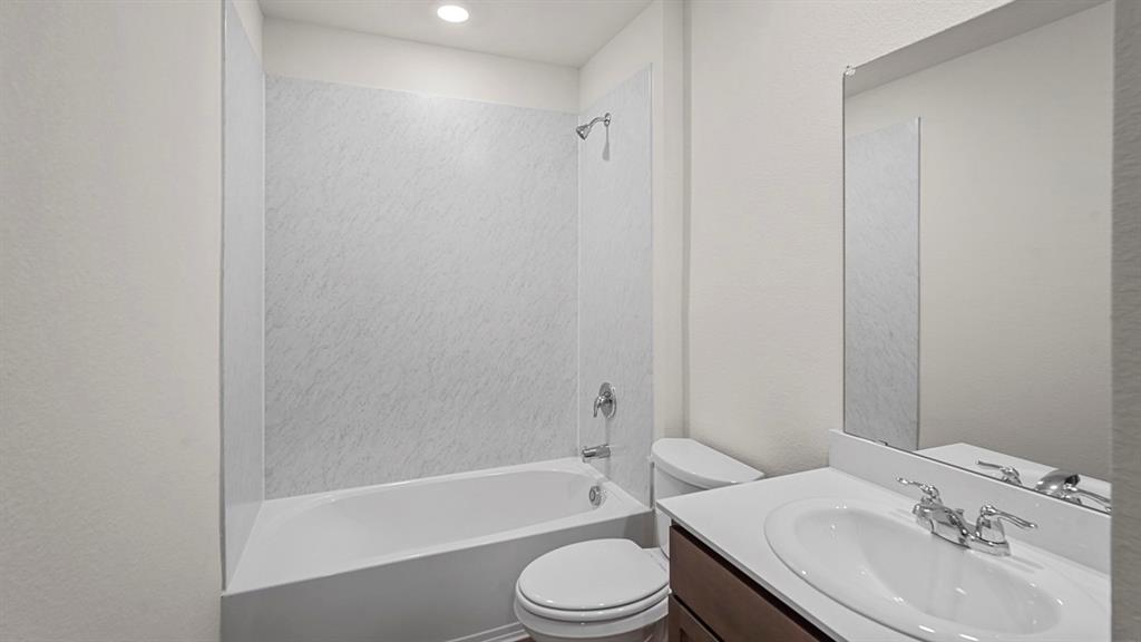 Bathroom featuring a shower and tub combination with surround paneling, vanity with a white countertop and oval sink, and a large wall-mounted mirror Bathroom featuring a shower and tub combination with surround paneling, vanity with a white countertop and oval sink, and a large wall-mounted mirror