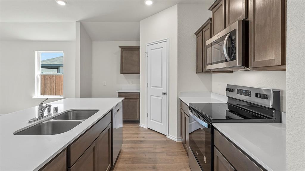 Kitchen featuring dark wood-finish cabinetry, white solid-surface countertops, stainless steel appliances, a double-basin undermount sink with a gooseneck faucet, and wood-finish flooring