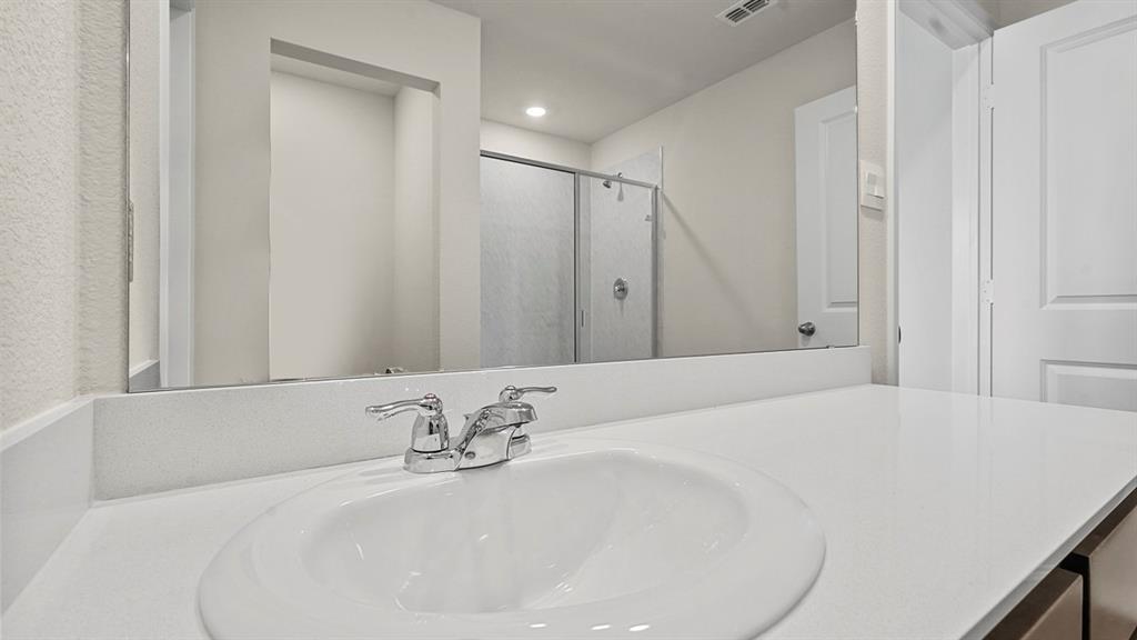 Bathroom featuring a solid-surface vanity countertop with an integrated oval sink, chrome dual-handle faucet, full-width mirror, and a walk-in shower enclosure