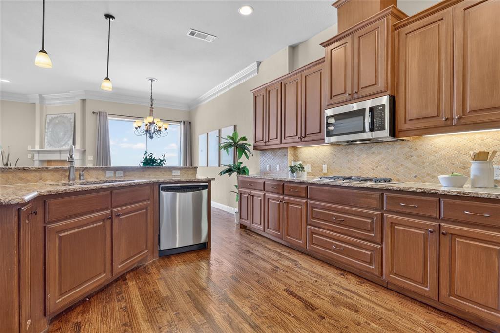 Kitchen featuring wood cabinetry, stone countertops, stone tile backsplash, stainless steel appliances, and wood-finish flooring