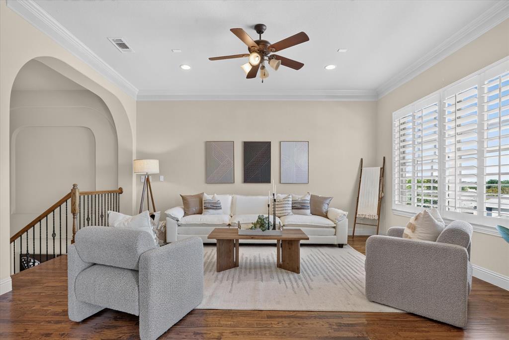 Living area featuring wood-finish flooring, crown molding, arched architectural detail, recessed lighting, and interior plantation shutters
