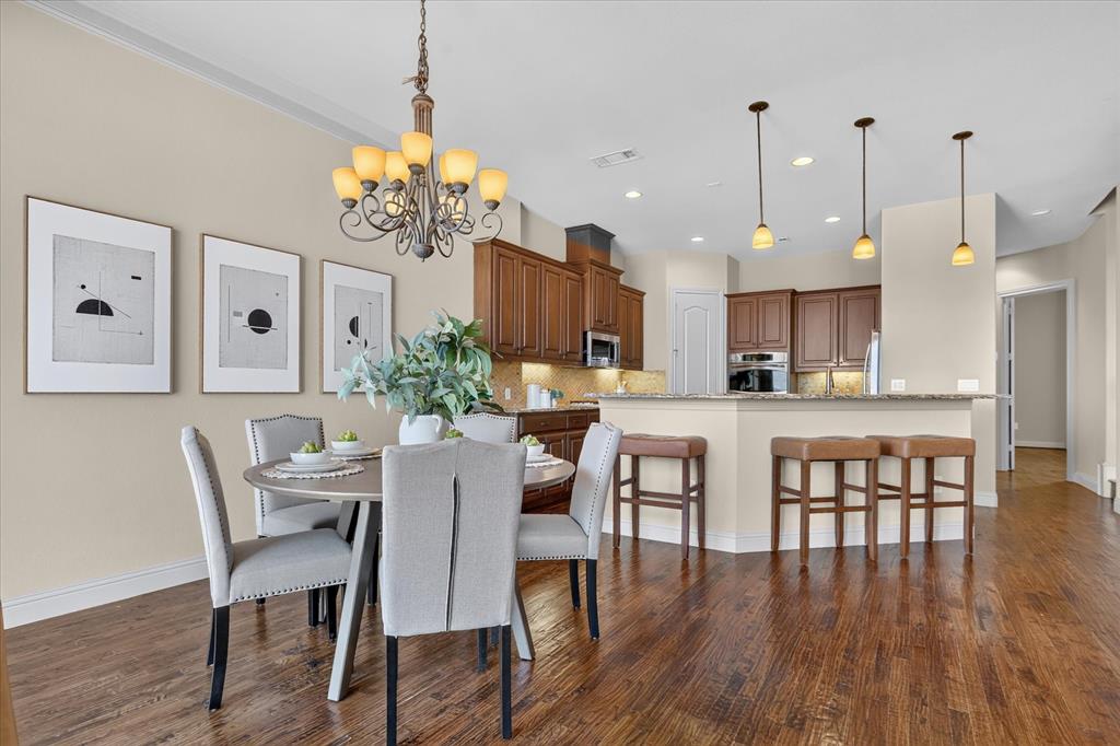 Open-concept kitchen featuring stained wood cabinetry, stone countertops, integrated recessed lighting, metal pendant fixtures, and wood-finish flooring throughout the dining area