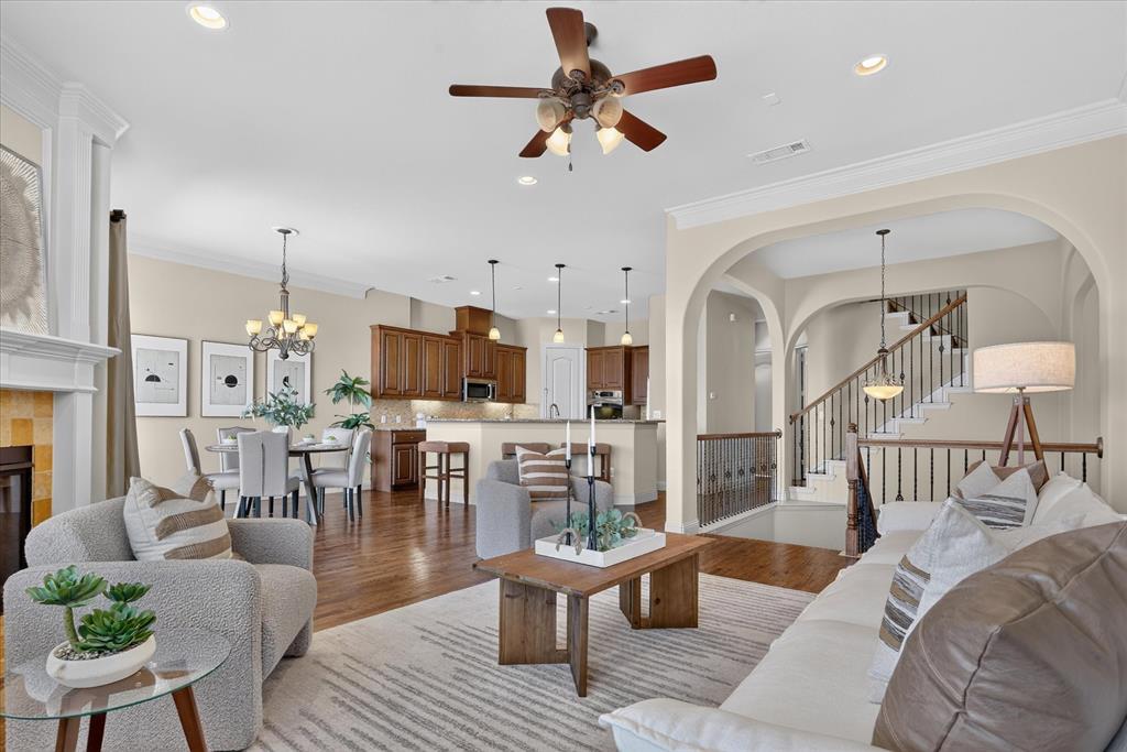 Open-concept floor plan featuring wood-finish flooring, recessed lighting, crown molding, arched room entries, and a fireplace with a traditional mantel