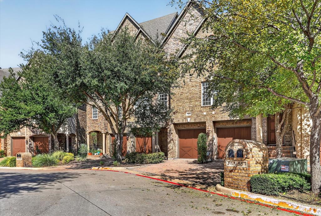 Multi-story brick exterior featuring steep gabled rooflines, stone-accented mailbox columns, and wood-finish garage doors