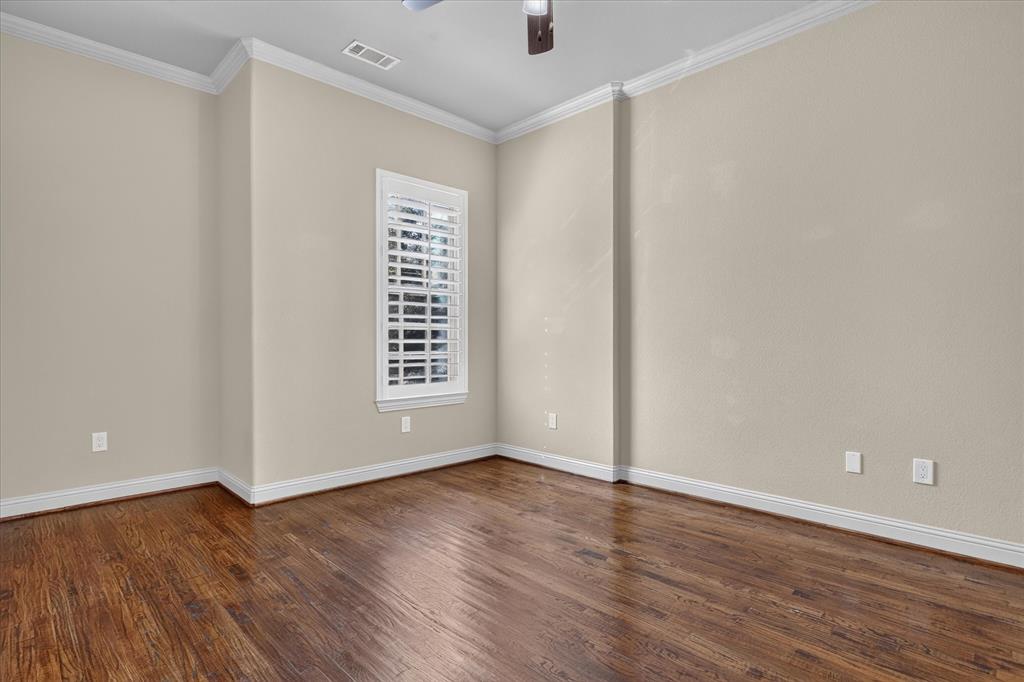 Interior room featuring wood-finish flooring, neutral wall paint, crown molding, and plantation shutters