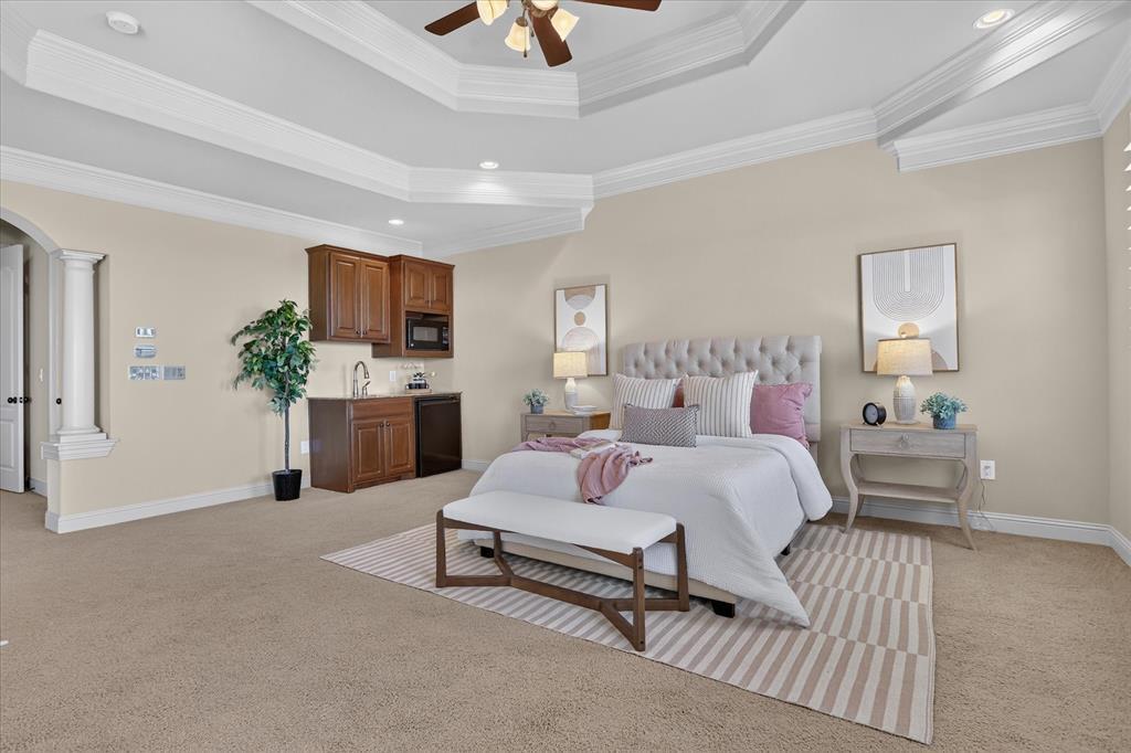 Tray ceiling with crown molding, built-in wet bar with cabinetry and integrated microwave, decorative architectural pillar, and recessed lighting