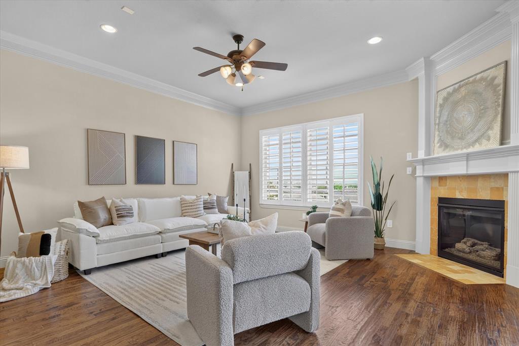 Living area featuring wood-finish flooring, crown molding, a fireplace with a stone-surround hearth, and plantation shutters
