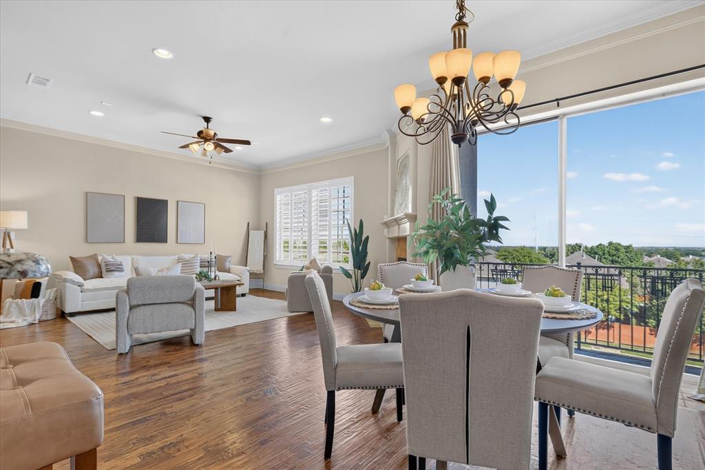 Open-concept living and dining area featuring wood-finish flooring, recessed lighting, crown molding, a decorative chandelier, and floor-to-ceiling windows with a black metal balcony railing
