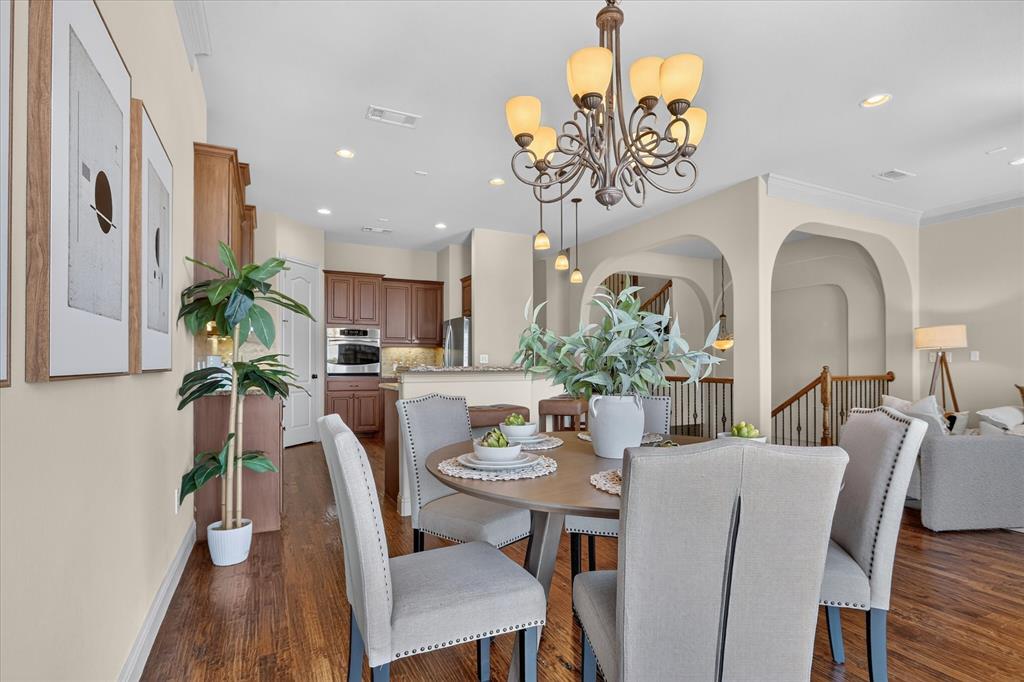 Open-concept dining area featuring dark wood-finish flooring, an ornate multi-light chandelier, arched architectural wall openings, and recessed lighting
