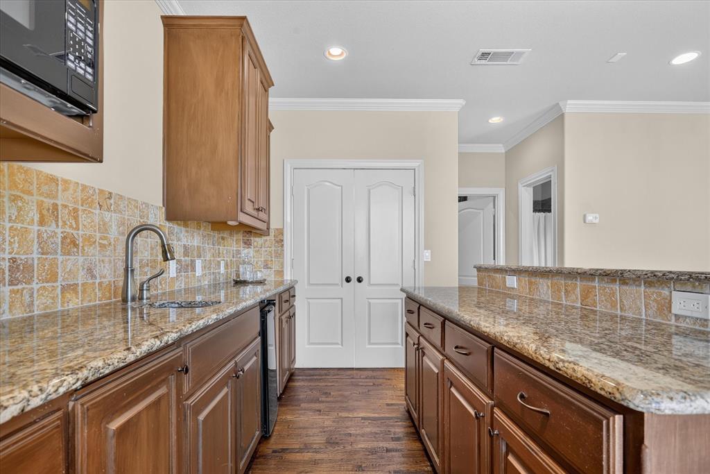 Wet bar kitchen featuring wood cabinetry, granite countertops, square-tile backsplash, built-in microwave, mini sink, and mini fridge. Handscraped wood flooring throughout.