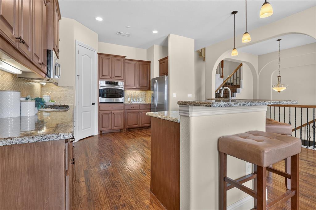 Kitchen featuring wood-finish cabinetry, stone countertops, a stainless steel built-in oven, pendant lighting, and wood-finish flooring