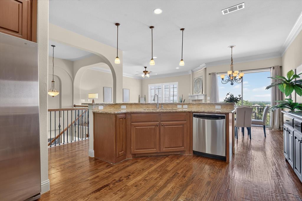 Kitchen featuring wood-finish flooring, a stone-surfaced island with a stainless steel dishwasher, pendant lighting, arched architectural details, and decorative crown molding