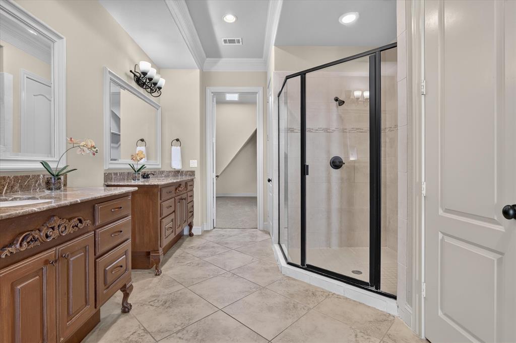 Dual wood cabinetry with stone-finish countertops, ceramic tile flooring, and a walk-in shower featuring a black-framed glass enclosure