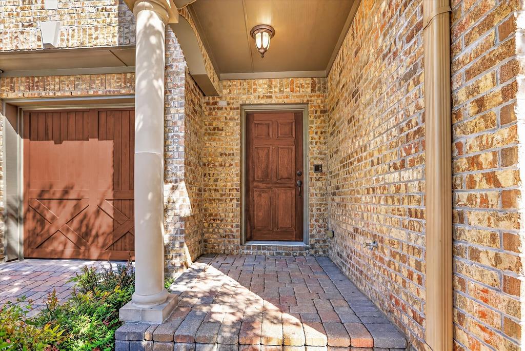 Brick exterior featuring a covered entryway, a wood-finish multi-panel door, a classic column, and a stone-paver porch