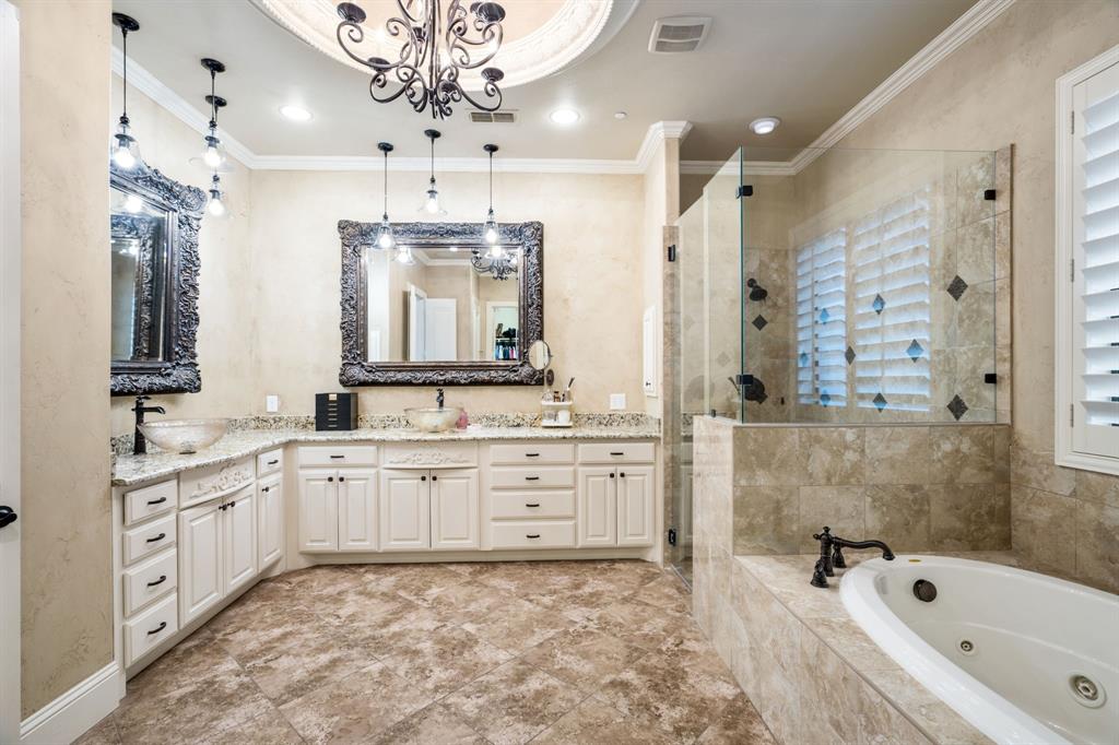 Bathroom featuring a double vanity with stone countertops and glass vessel sinks, stone tile flooring, a jetted soaking tub, and a glass-enclosed shower with stone tile surround