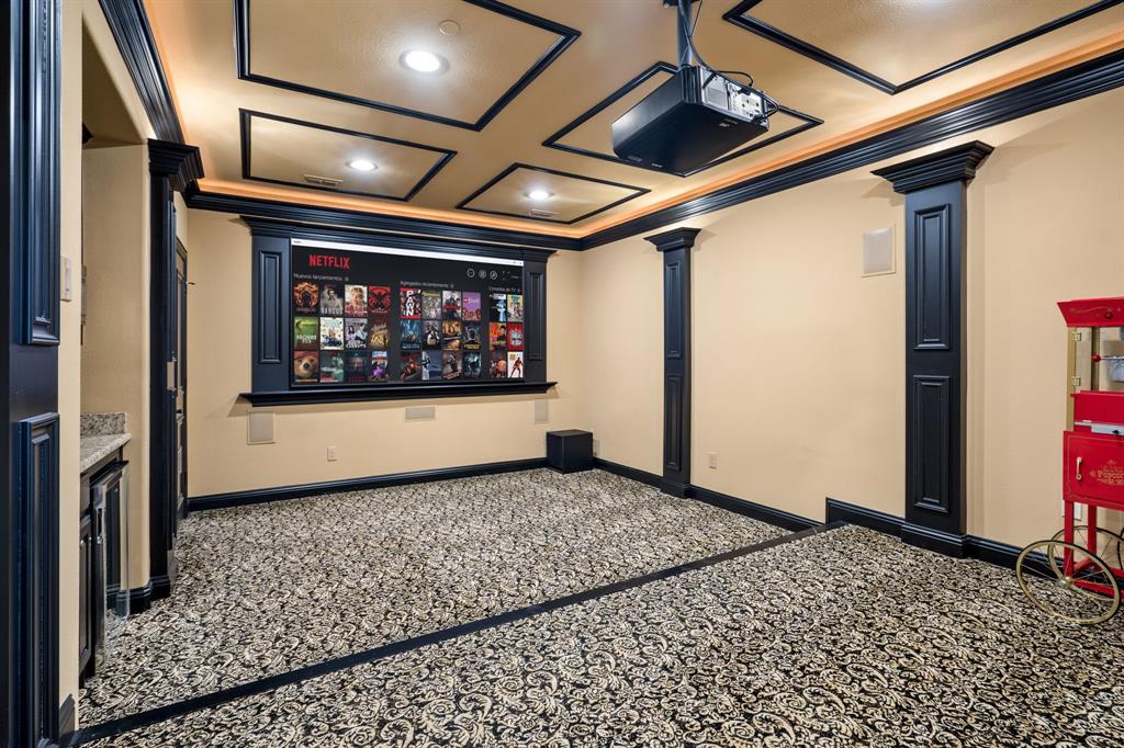 Dedicated media room featuring a coffered ceiling, recessed lighting, built-in display cabinetry, decorative columns, and a fixed projector mount