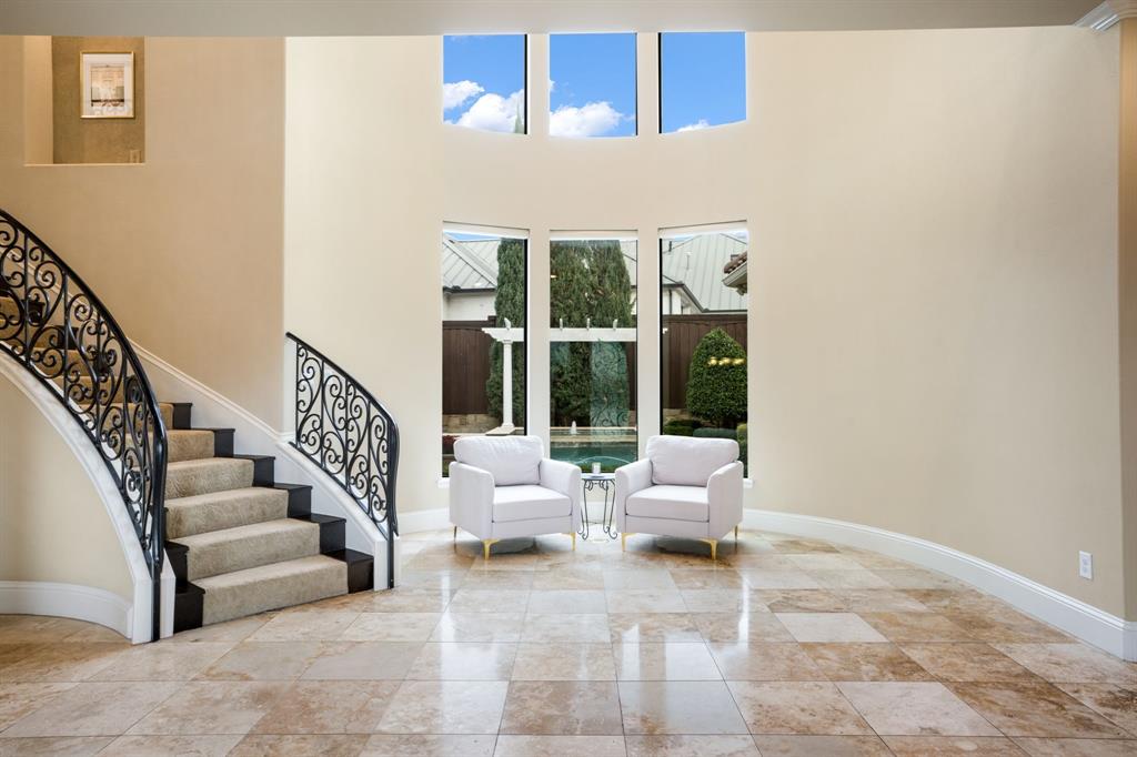 Grand foyer featuring soaring ceilings, a curved staircase with decorative wrought-iron railings, stone-tile flooring, and expansive windows