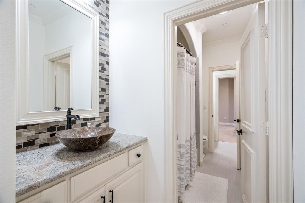 Vanity featuring a stone-composite countertop, stone vessel sink, and matte black faucet, accented by a decorative linear glass-tile backsplash and framed mirror