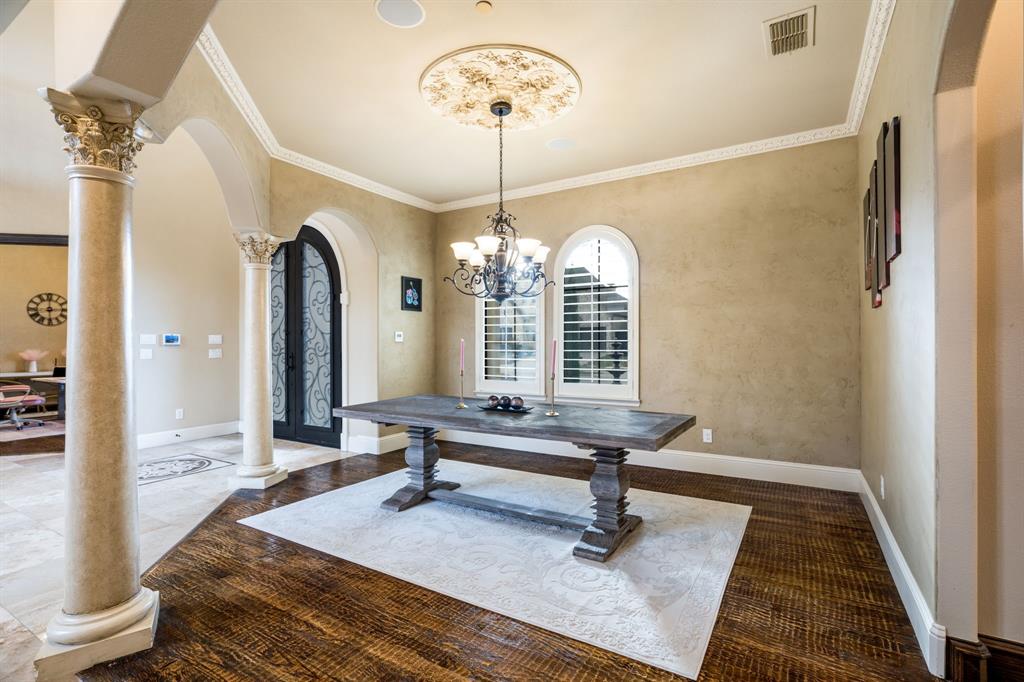 Formal dining area featuring decorative ceiling medallion, arched windows with plantation shutters, custom wrought iron entryway door, and architectural columns with ornate capitals