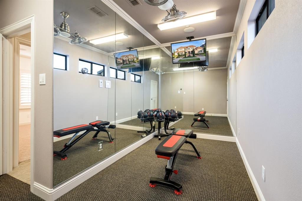 Full-length mirrored wall, high-set horizontal windows, wall-mounted television, neutral carpeting, and ceiling-mounted light fixtures