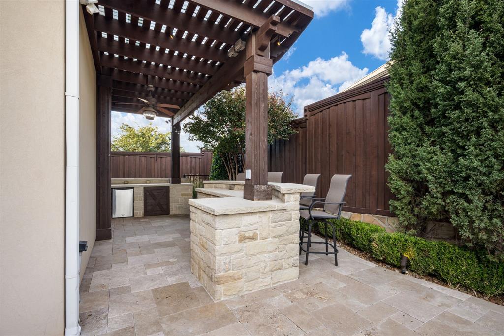 Outdoor living area featuring a covered pergola, stone-clad bar, built-in cabinetry, tile patio flooring, and stained wood privacy fencing