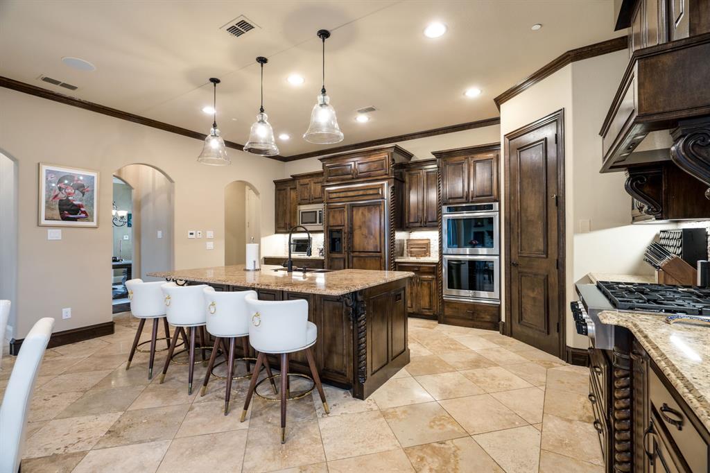Kitchen featuring custom wood cabinetry, central island with stone countertop, built-in stainless steel double wall ovens, natural stone tile flooring, and decorative pendant lighting