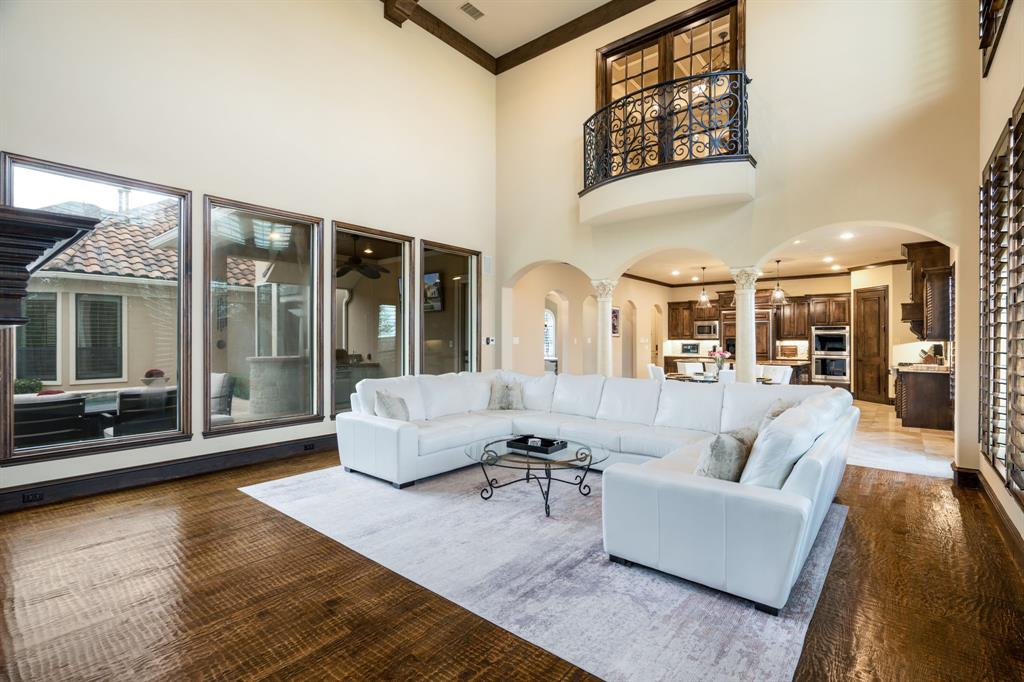 Vaulted ceilings, expansive floor-to-ceiling windows, arched architectural entries with decorative columns, and an upper-level interior balcony featuring custom wrought-iron railings