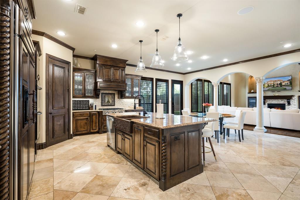 Kitchen featuring custom wood cabinetry, an expansive center island with a farmhouse sink, stone countertops, stone flooring, and decorative column accents