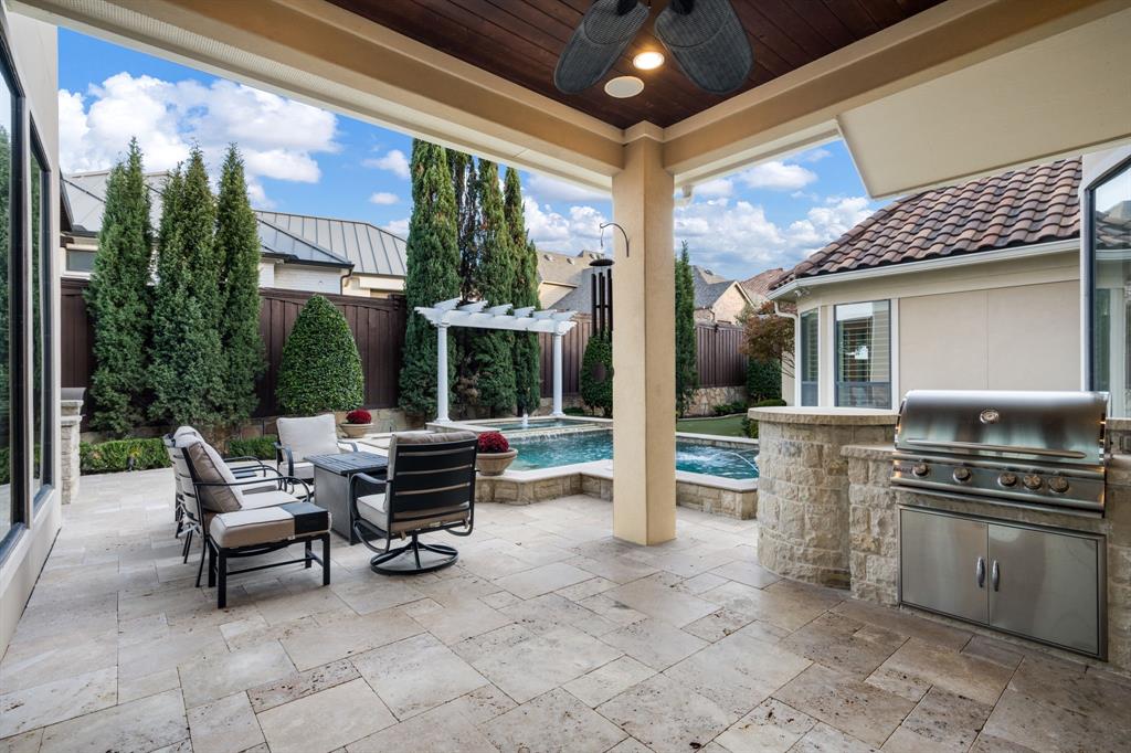 Covered patio featuring stone tile flooring, a wood-paneled ceiling, a built-in stainless steel outdoor grill, and a swimming pool with a pergola