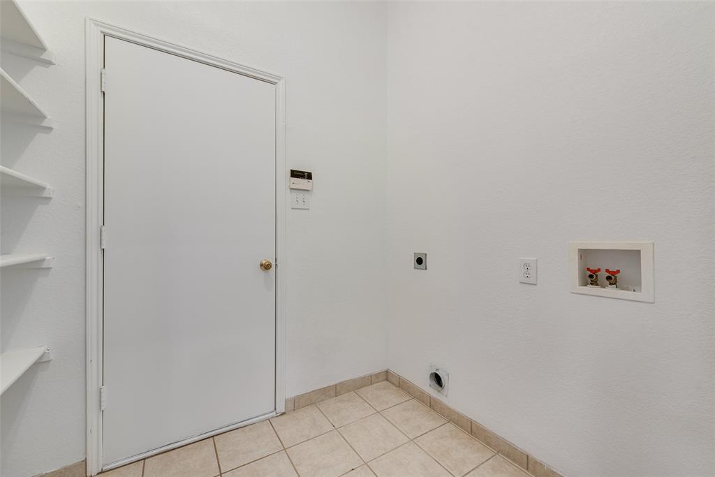 Utility space featuring ceramic tile flooring, built-in wall shelving, and dedicated hookups for laundry appliances