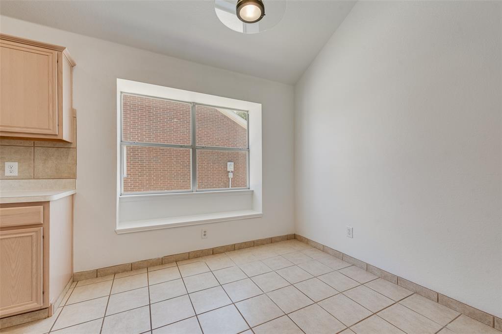 Vaulted ceiling, inset window with a built-in sill, light-toned wood cabinetry, and ceramic tile flooring