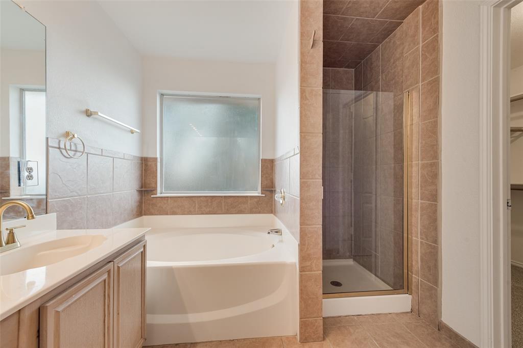 Bathroom featuring a soaking tub, separate tiled shower enclosure with glass door, vanity with a rectangular basin, and neutral-toned wall tiling