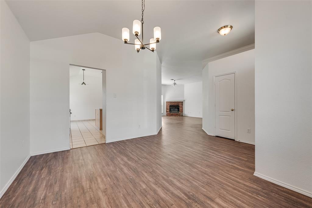 Open dining area featuring vaulted ceilings, wood-finish flooring, a multi-arm chandelier, and a masonry fireplace Open dining area featuring vaulted ceilings, wood-finish flooring, a multi-arm chandelier, and a masonry fireplace