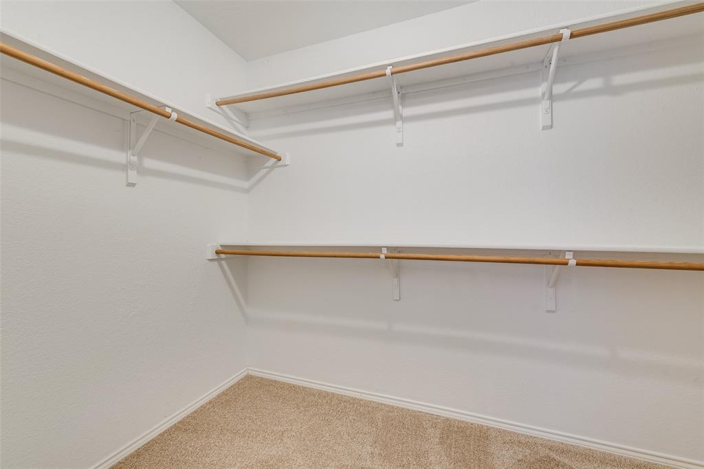 Walk-in storage space featuring multi-level white shelving and integrated wooden garment rods, complemented by wall-to-wall carpeting