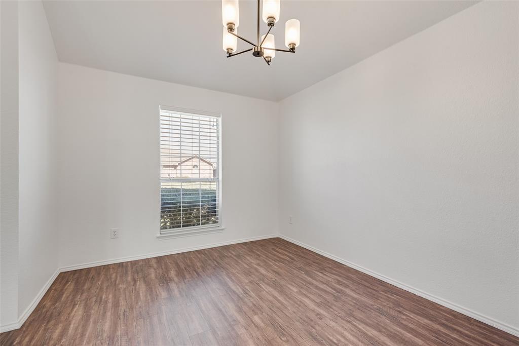 Room featuring wood-finish flooring, a neutral color palette, a single window with horizontal blinds, and a five-light tiered chandelier with a metallic finish Room featuring wood-finish flooring, a neutral color palette, a single window with horizontal blinds, and a five-light tiered chandelier with a metallic finish
