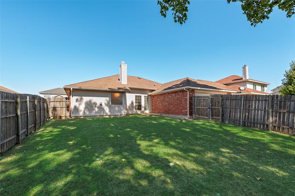 Backyard featuring a grass lawn, perimeter wood fencing, masonry chimney, and brick exterior accents