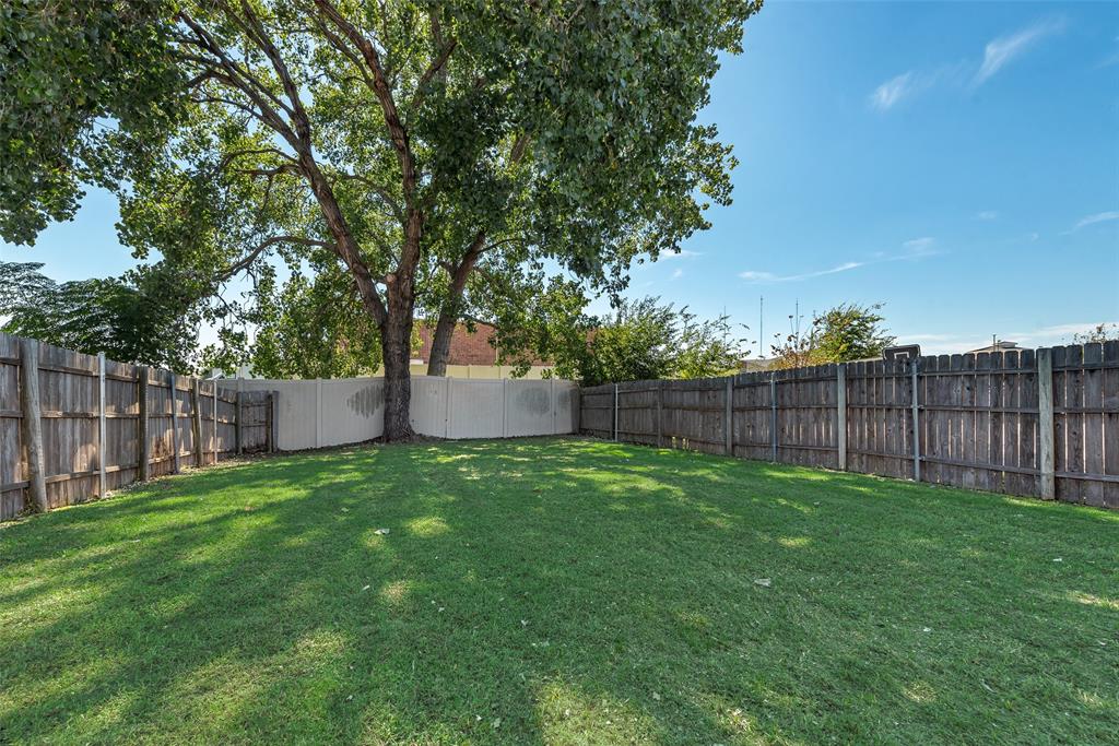Expansive backyard featuring a grass lawn, mature trees, and perimeter wood and vinyl fencing