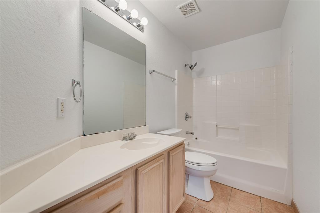 Bathroom featuring a light wood-finish vanity, solid-surface countertop, full-height wall mirror, four-light vanity fixture, and a tiled shower surround