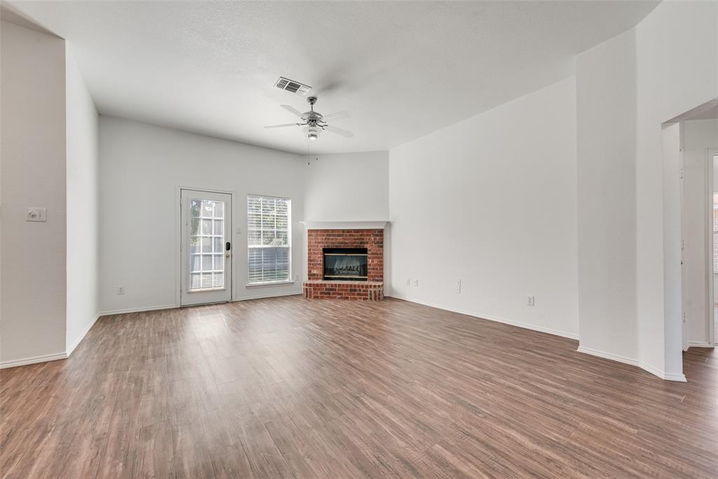 Living area featuring wood-finish flooring, vaulted ceilings, brick fireplace with mantel, ceiling fan, and access to the exterior Living area featuring wood-finish flooring, vaulted ceilings, brick fireplace with mantel, ceiling fan, and access to the exterior