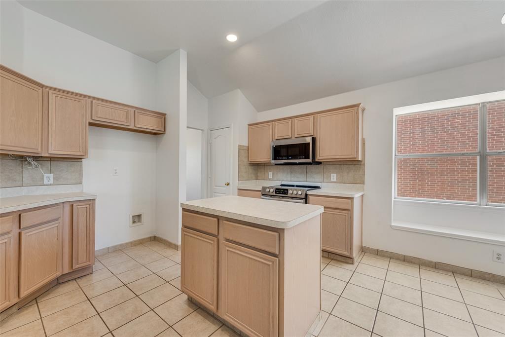 Kitchen featuring light-finish cabinetry, a center island with a solid surface countertop, ceramic tile flooring, built-in stainless steel microwave, and a recessed window ledge Kitchen featuring light-finish cabinetry, a center island with a solid surface countertop, ceramic tile flooring, built-in stainless steel microwave, and a recessed window ledge