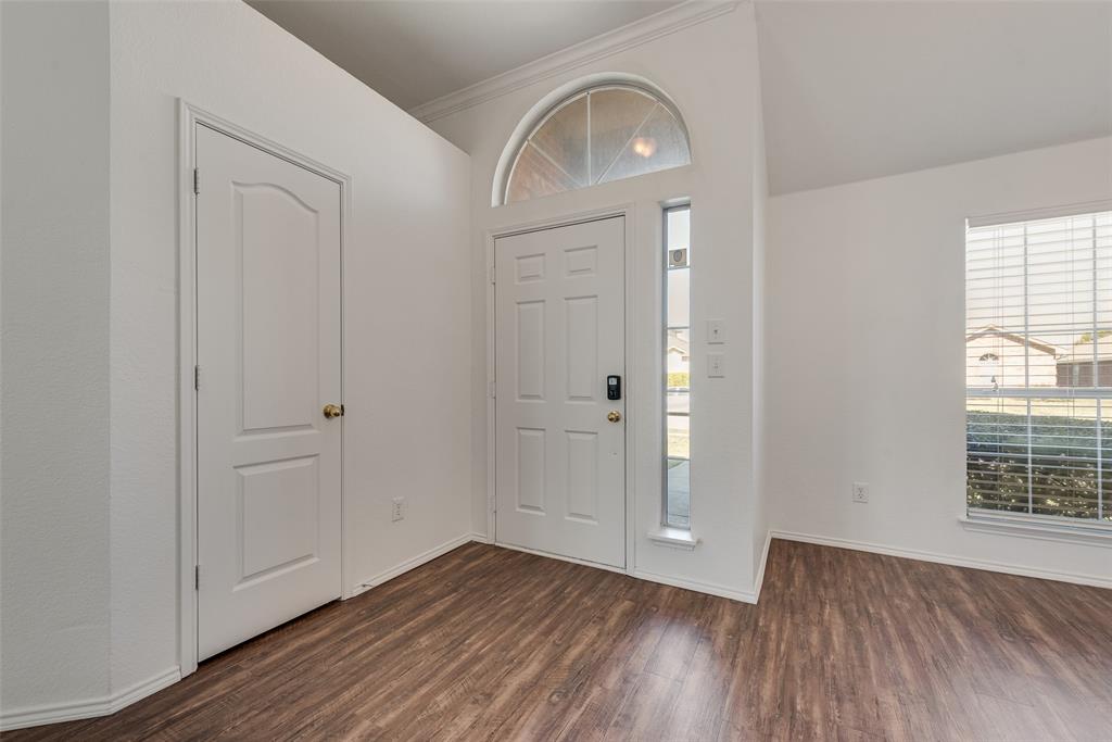 Entryway featuring wood-finish flooring, vaulted ceilings, a six-panel front door with an arched transom window, a vertical sidelight, and a large window with blinds Entryway featuring wood-finish flooring, vaulted ceilings, a six-panel front door with an arched transom window, a vertical sidelight, and a large window with blinds