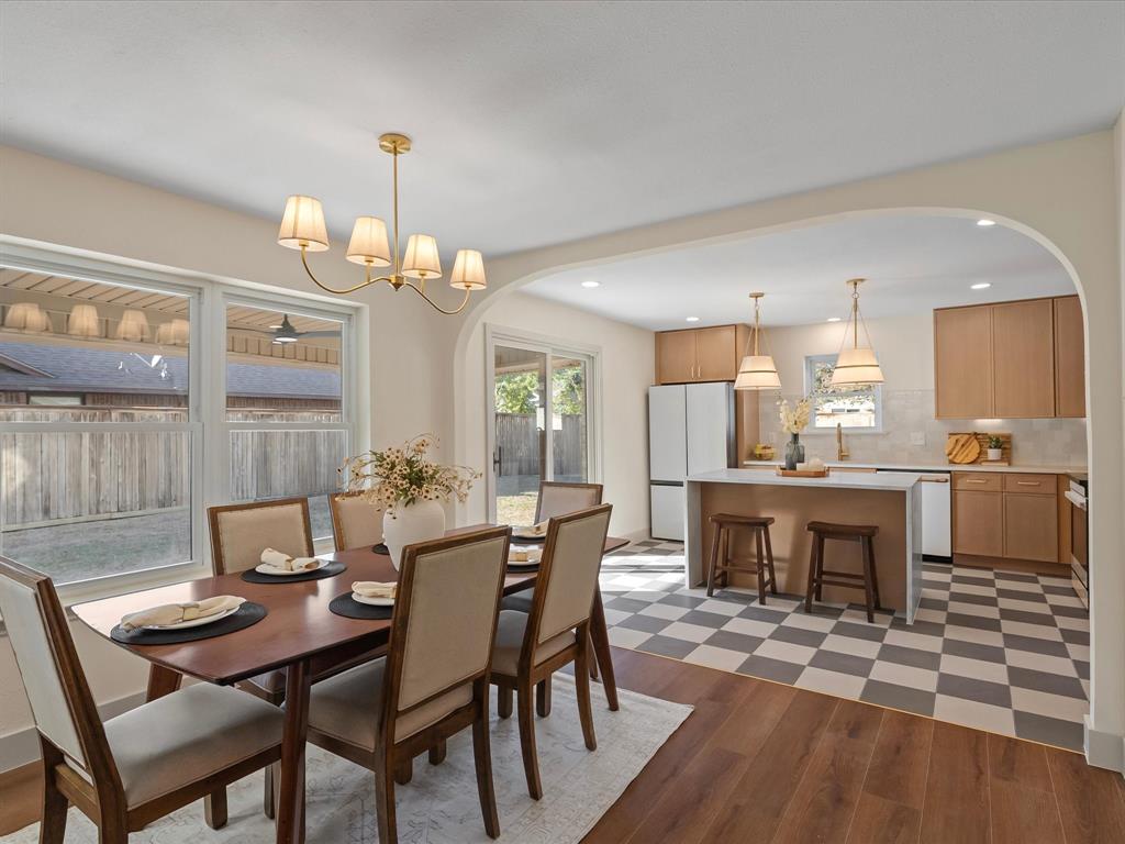 Kitchen and dining area featuring an arched architectural opening, wood-finish cabinetry, central island with seating, checkerboard tile flooring, and multi-light chandelier fixtures Kitchen and dining area featuring an arched architectural opening, wood-finish cabinetry, central island with seating, checkerboard tile flooring, and multi-light chandelier fixtures