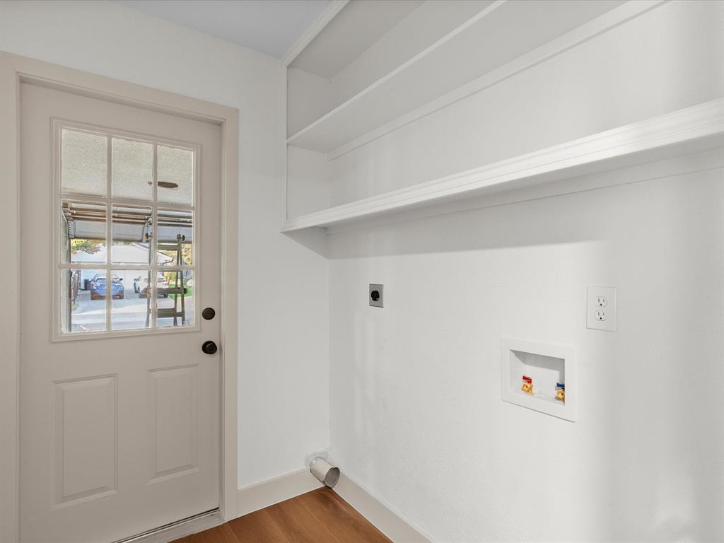 Service area featuring built-in wall shelving, laundry hookups, and a glass-paneled exterior door with wood-finish flooring