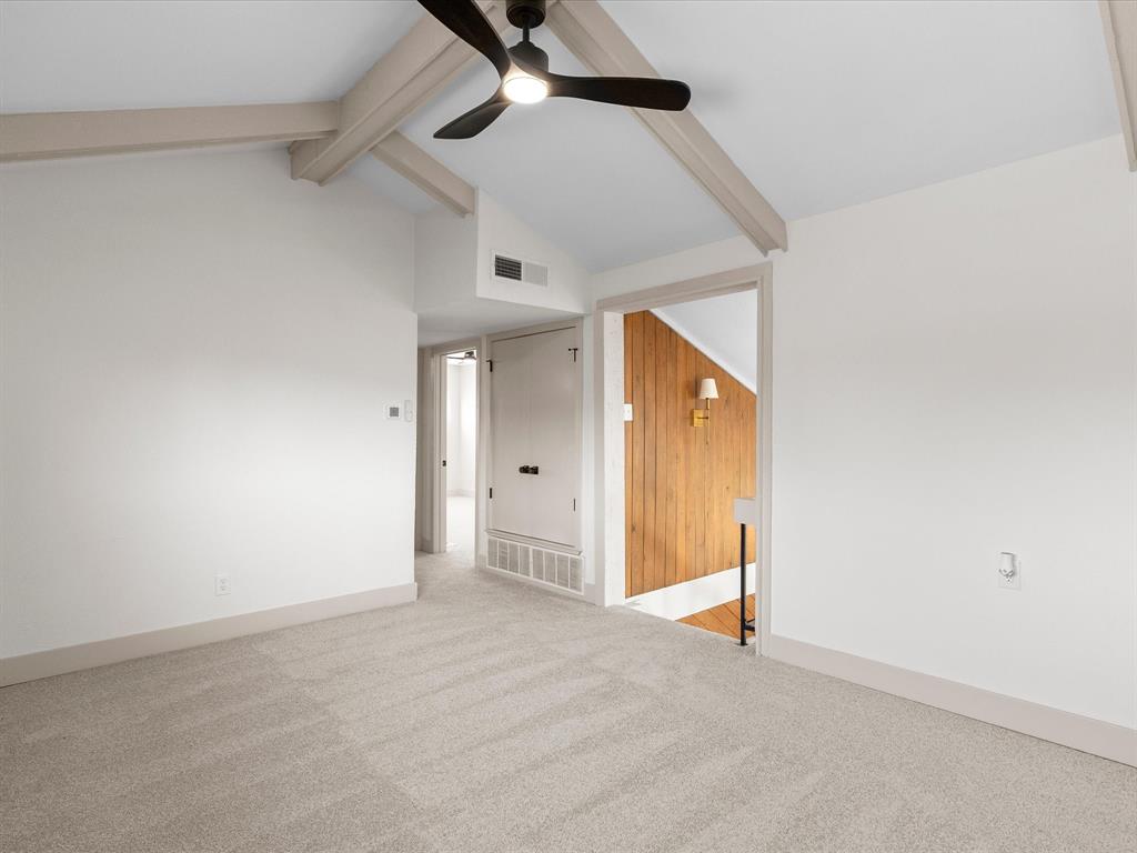 Vaulted ceiling featuring exposed beams, neutral carpeting, and a central ceiling fan with integrated lighting